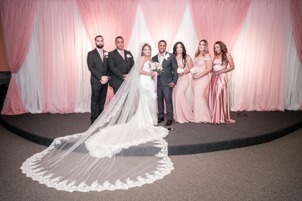 bride and groom with groomsmen and bridesmaids in long pink dresses in front of pink and white curtains